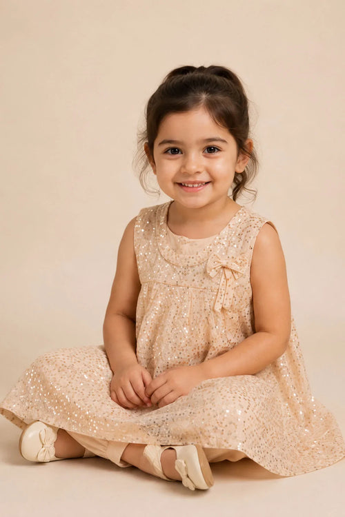 Adorable toddler in sparkly beige dress with bow, perfect for kids' fashion and special occasions.