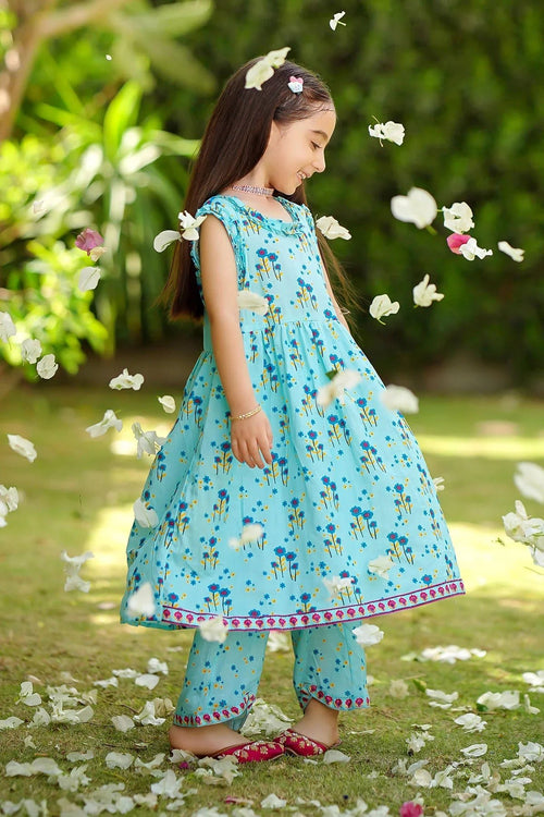 Girl in blue floral dress and matching pants, playing outdoors with falling petals