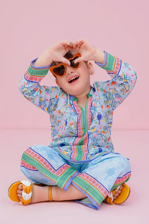Happy child in colorful floral print kids outfit with heart sunglasses, sitting on pink background