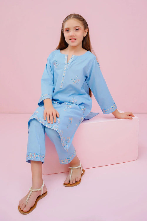 Girl in light blue embroidered kurta set with pearl sandals, sitting on pink block