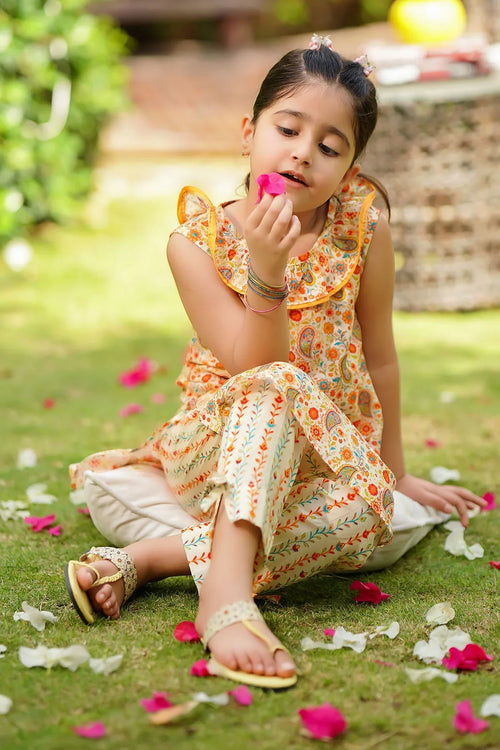 Little girl in floral print dress sitting on grass with flower petals, wearing sandals