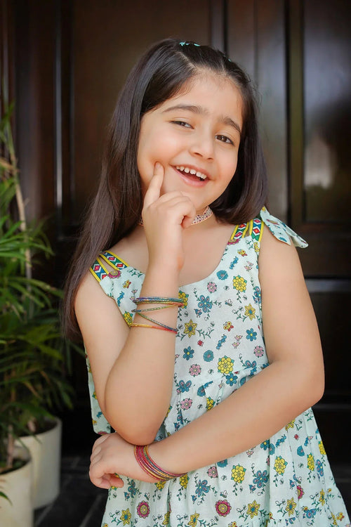 Smiling girl in floral print dress with colorful bangles, perfect for kids' fashion