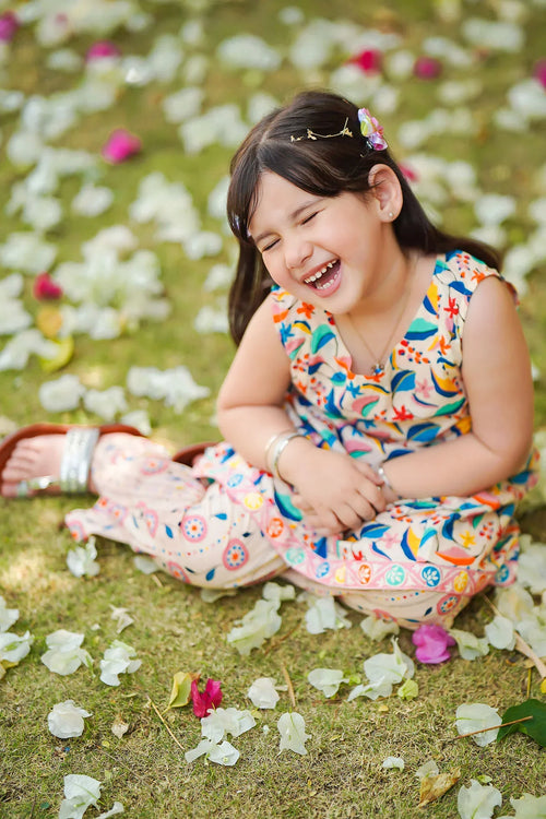 Happy girl laughing in colorful floral dress, sitting on grass with flower petals, perfect for kids fashion