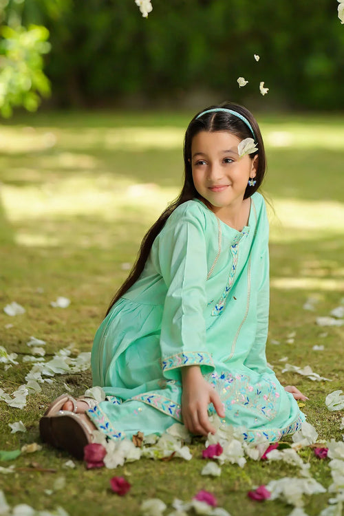 Girl in mint green embroidered dress sitting on grass with flower petals, perfect for kids fashion